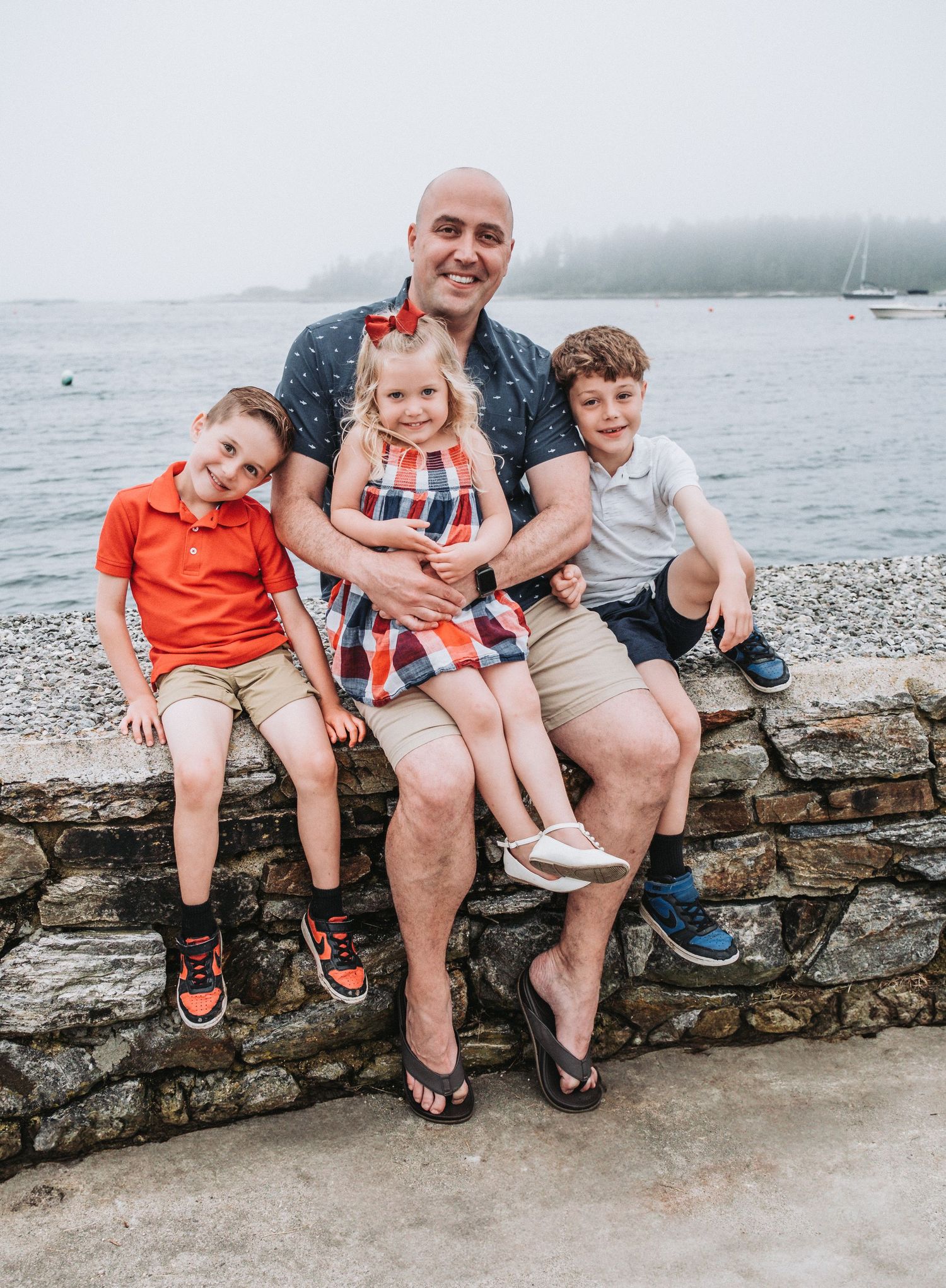A Dad and his three young children sit atop a rock wall at the Sebasco Harbor Resort in Phippsburg, Maine.