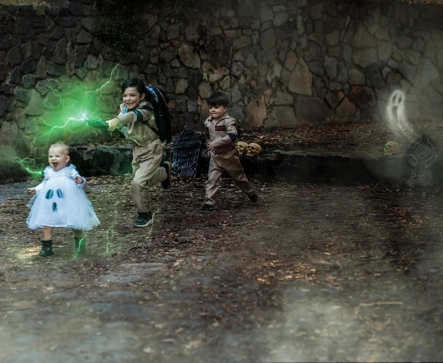 Three children in Ghostbusters Halloween costumes chase glowing ghosts in a spooky stone tunnel setting.