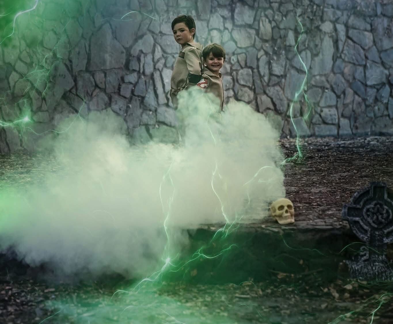 Two boys stand above glowing green lightning and mystical smoke near a stone wall with a skull prop.
