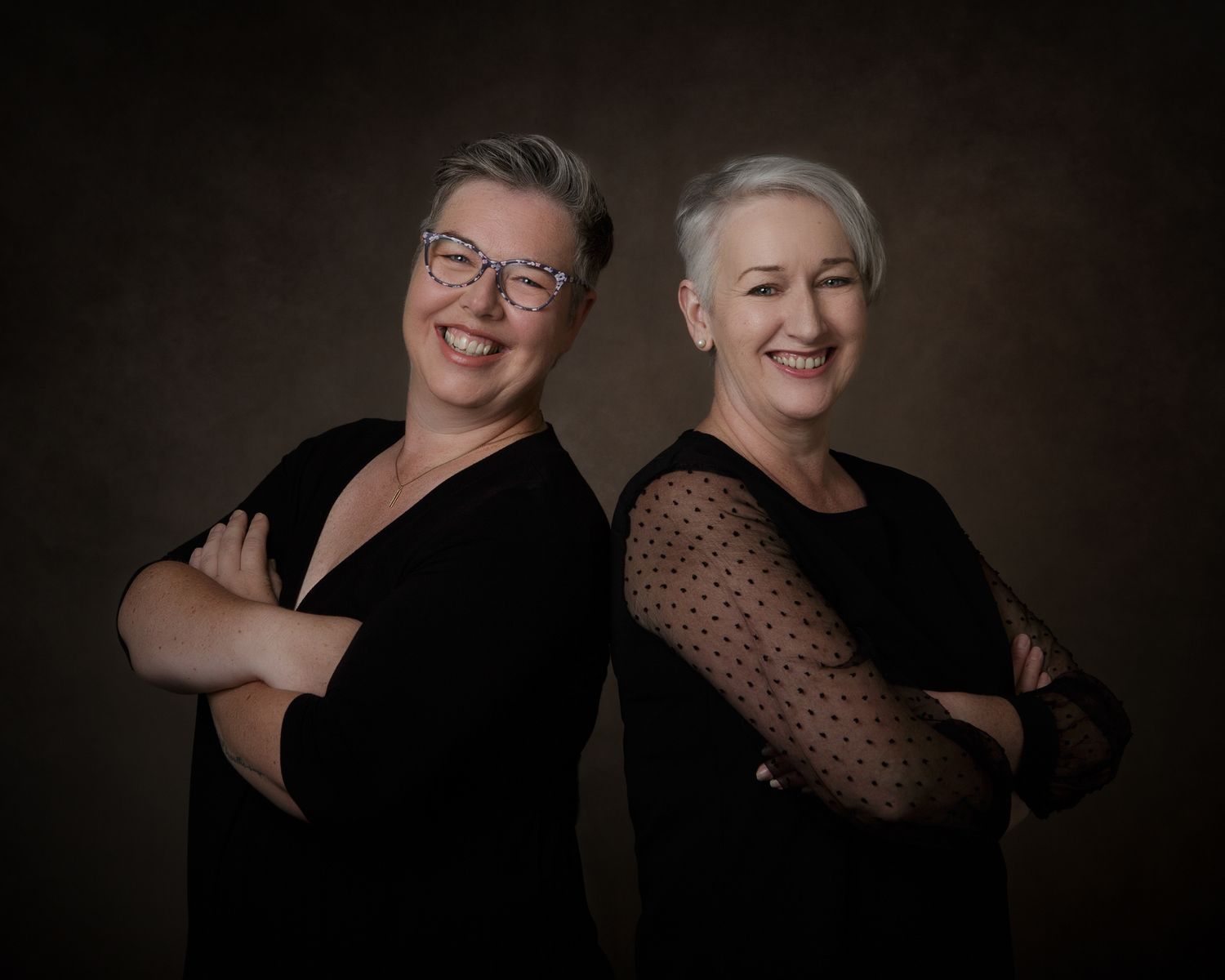 two business women dressed in dark clothes against a dark background for a business profile photo