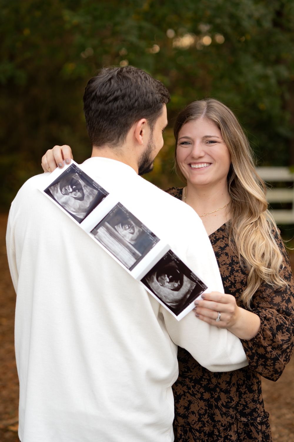 Women holding up her ultrasound with her arms wrapped around her husband
