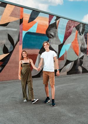 Couple poses in front of vibrant geometric wall mural showing sequence of progressive motion and interaction.