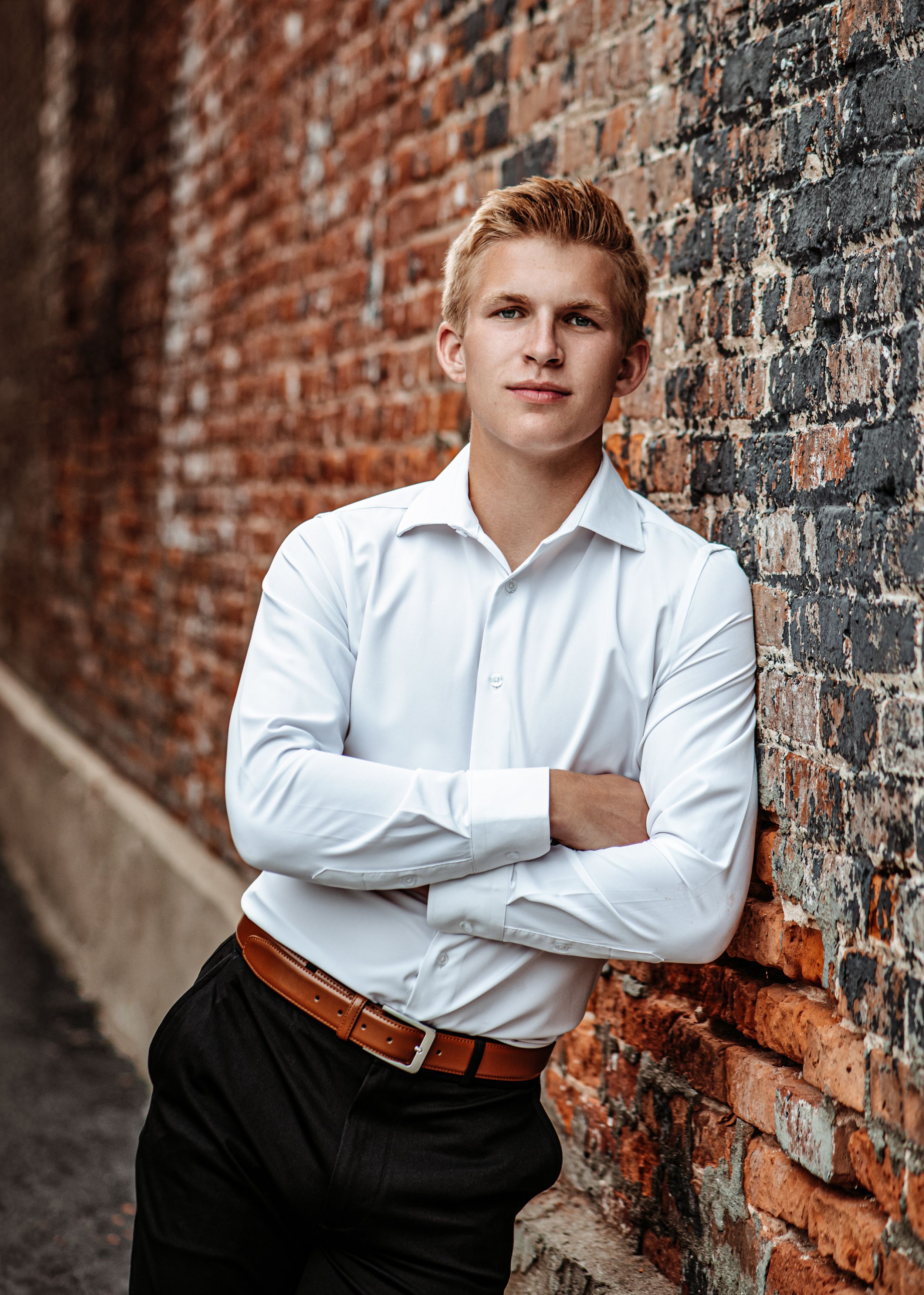 Professional portrait against brick wall featuring white dress shirt and classic styling.