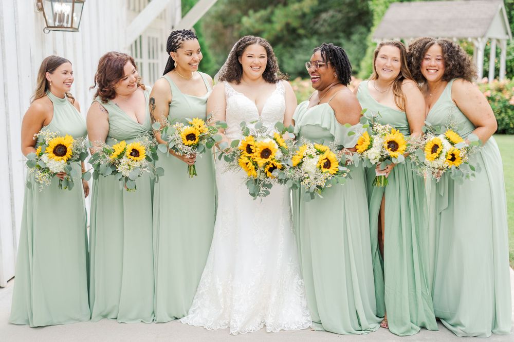 A wedding party wearing mint green bridesmaid dresses holds vibrant yellow sunflower bouquets beside the bride in white.