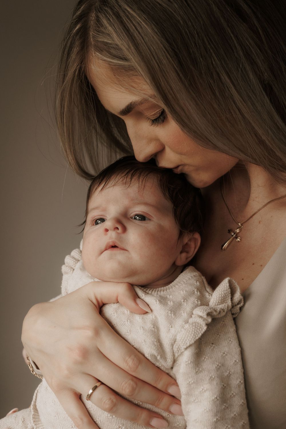 Ein zärtlicher Moment zeigt eine Mutter, die ihr in eine cremefarbene Decke gewickeltes Baby hält und streichelt.