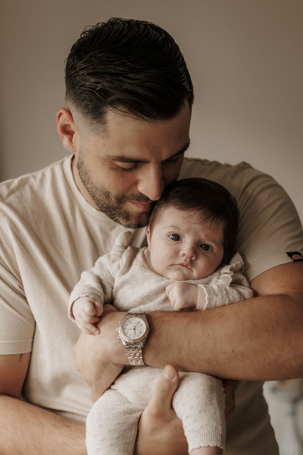 Ein zärtlicher Moment, eingefangen in warmen Tönen, ein Elternteil wiegt ein kleines Baby in weicher weißer Kleidung