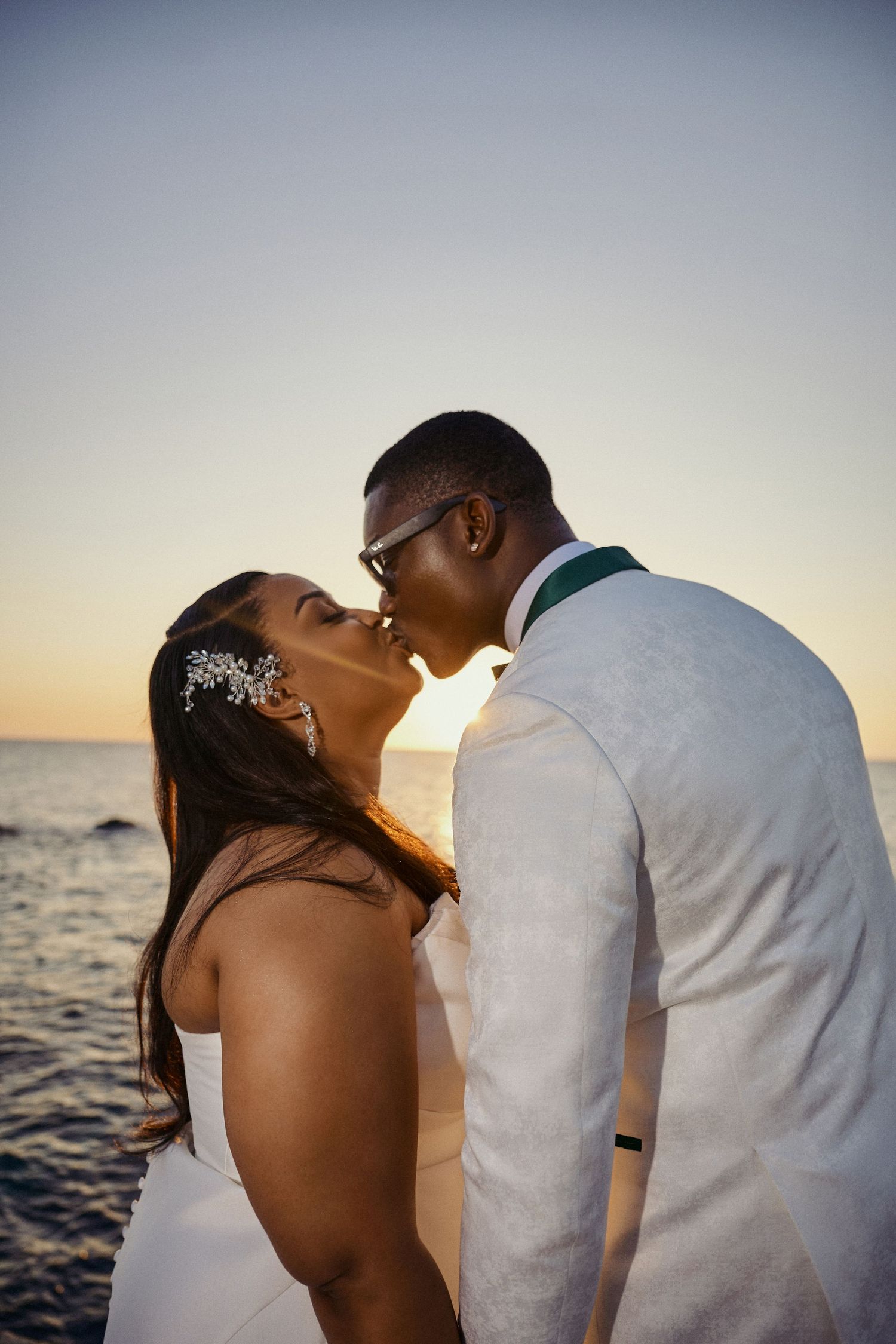 A couple shares an intimate moment together at their outdoor wedding, wearing a navy blue suit by Jamaica Wedding Photographer