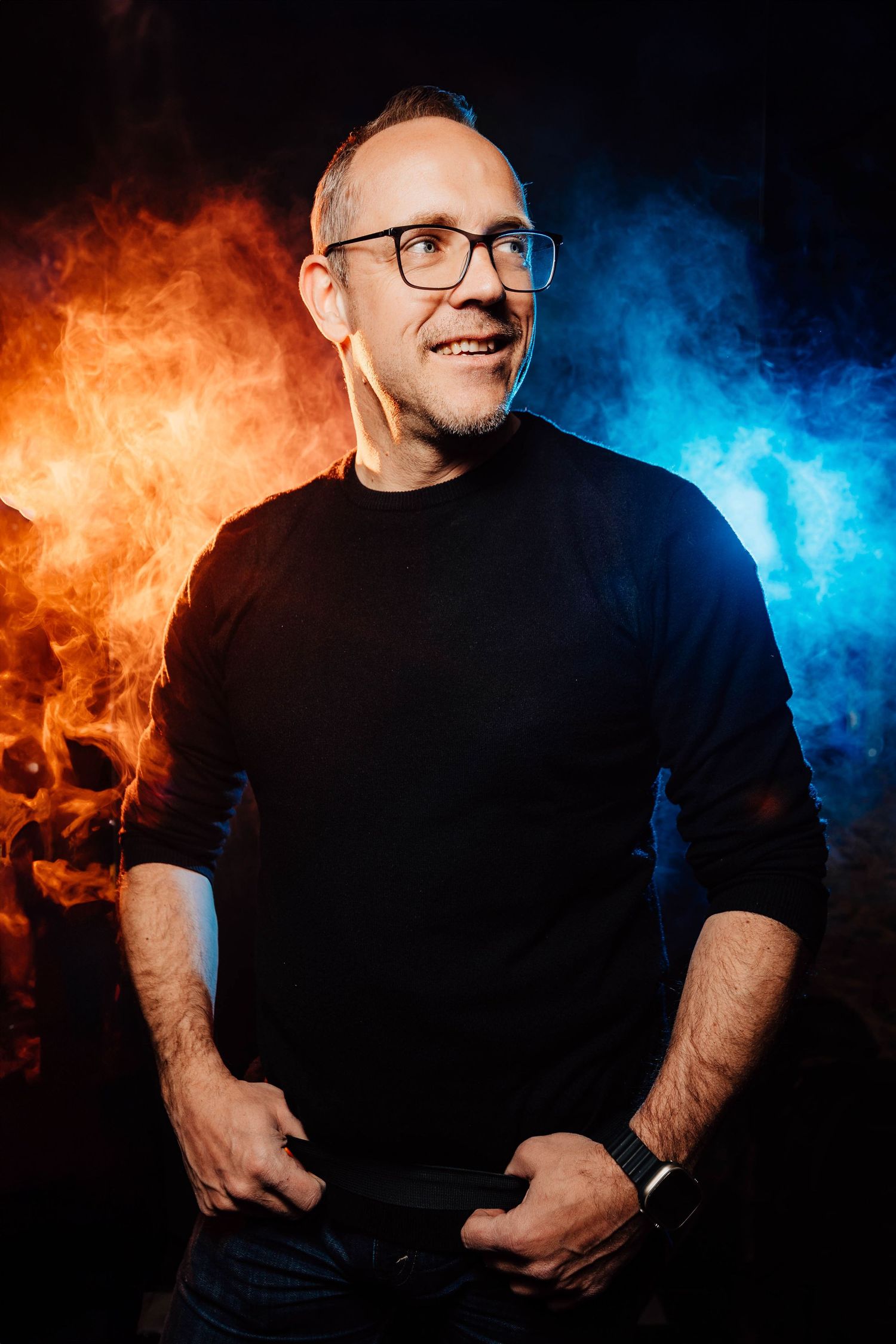 Portrait professionnel de photographe avec fumée orange et bleue, souriant, en pull noir et lunettes