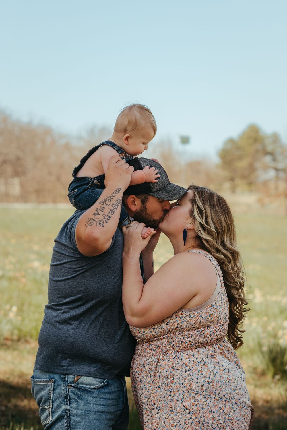 Joyful family moment outdoors with baby sitting on shoulders in sunny field.