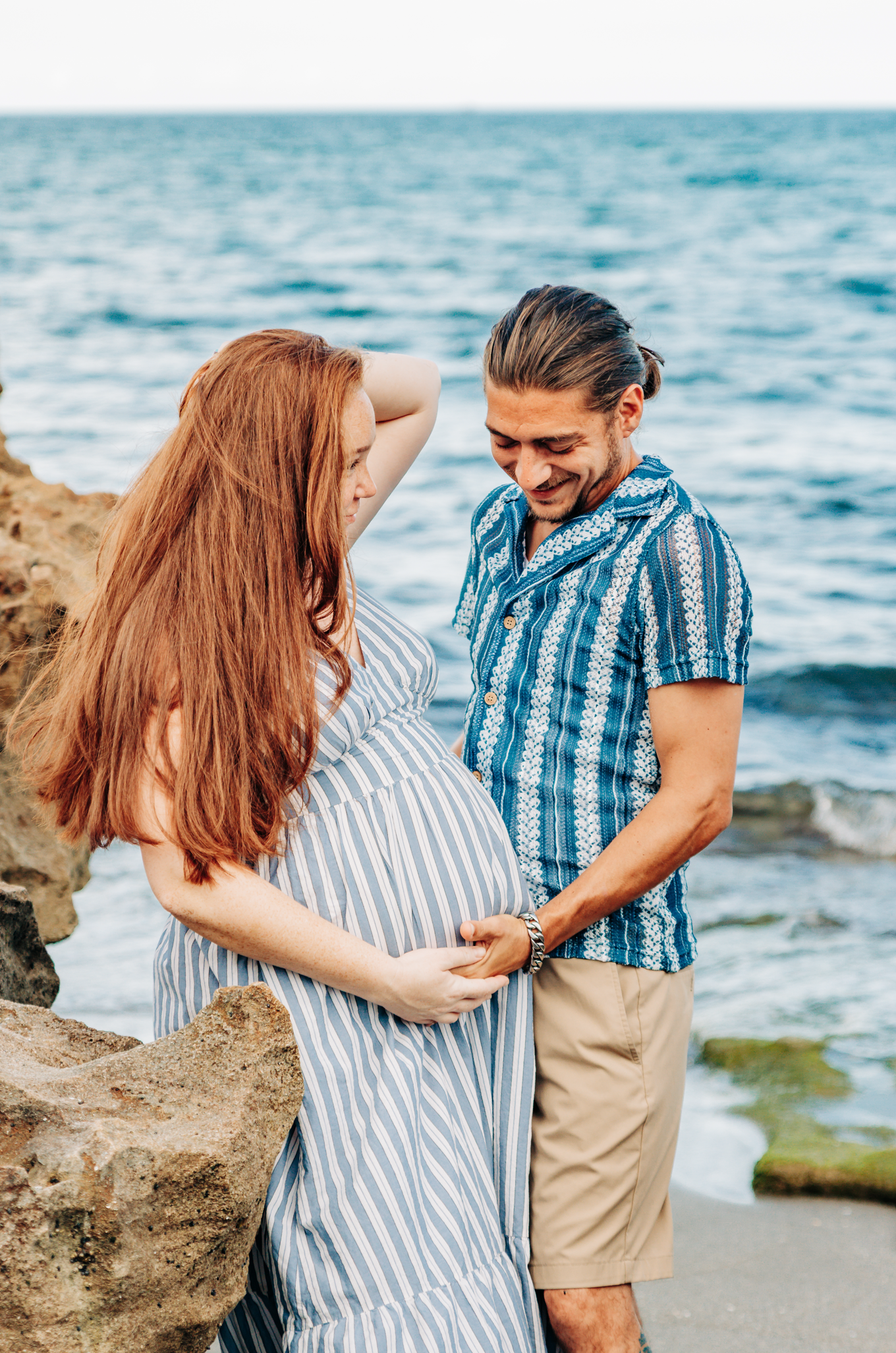 Maternity photographer Palm Beach County portrait of an expecting couple together on the rocky shoreline at Coral Cove Beach in Jupiter.
