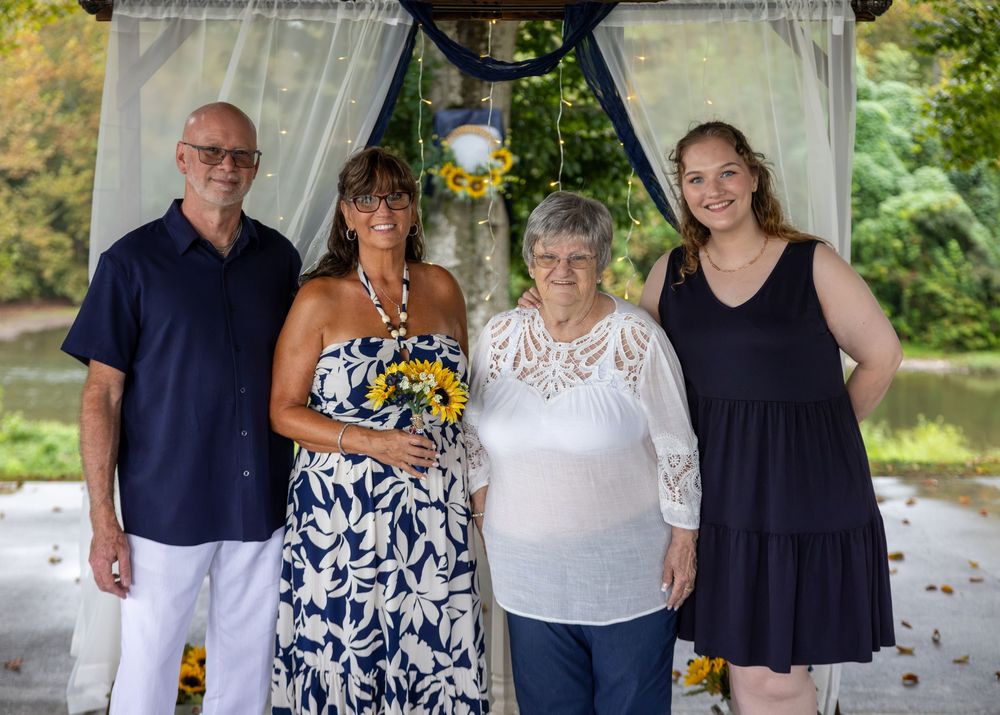 Family of four posing outdoors under floral arch at a wedding celebration with sunflowers.