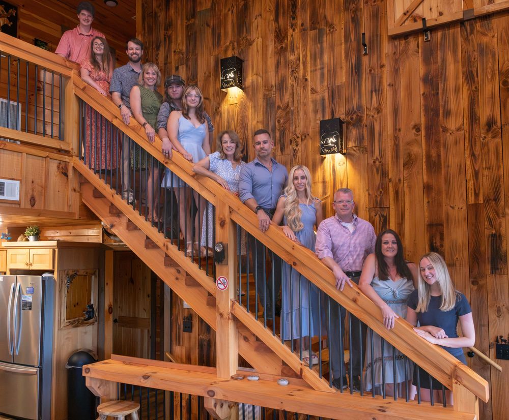 Group of people posing on wooden staircase inside a rustic log cabin home with warm lighting.