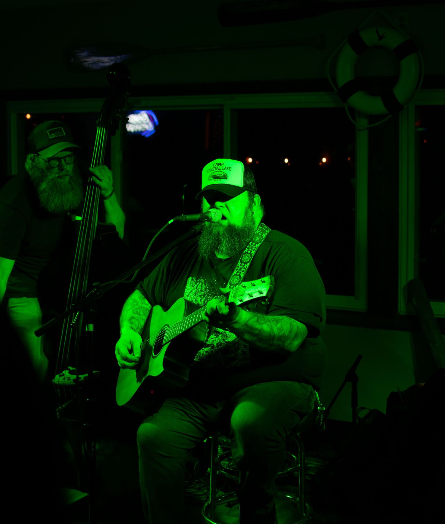 Bearded musician performing with acoustic guitar under green stage lighting at live music venue.