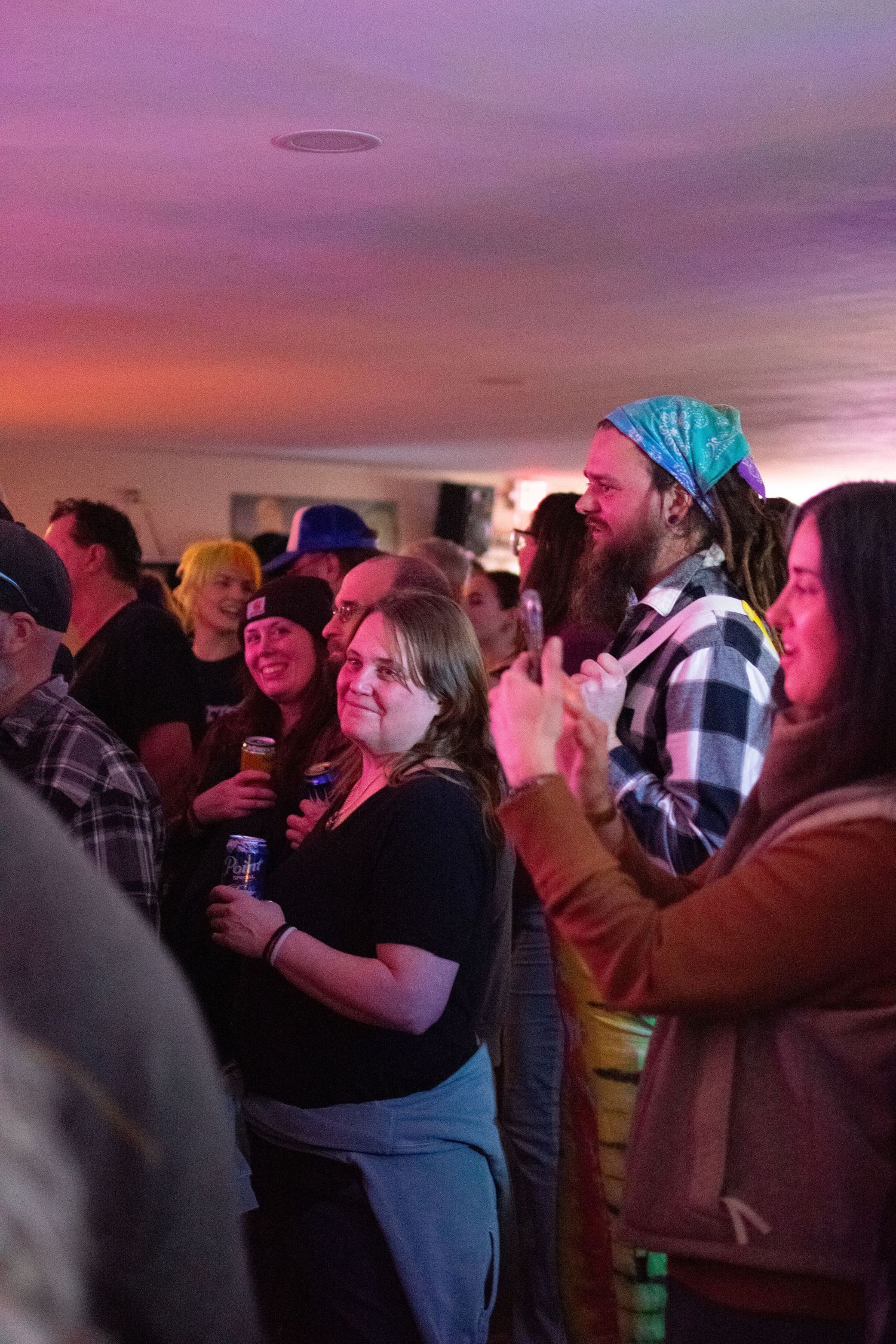Diverse crowd enjoying live music event under pink and purple ambient lighting at indoor venue.