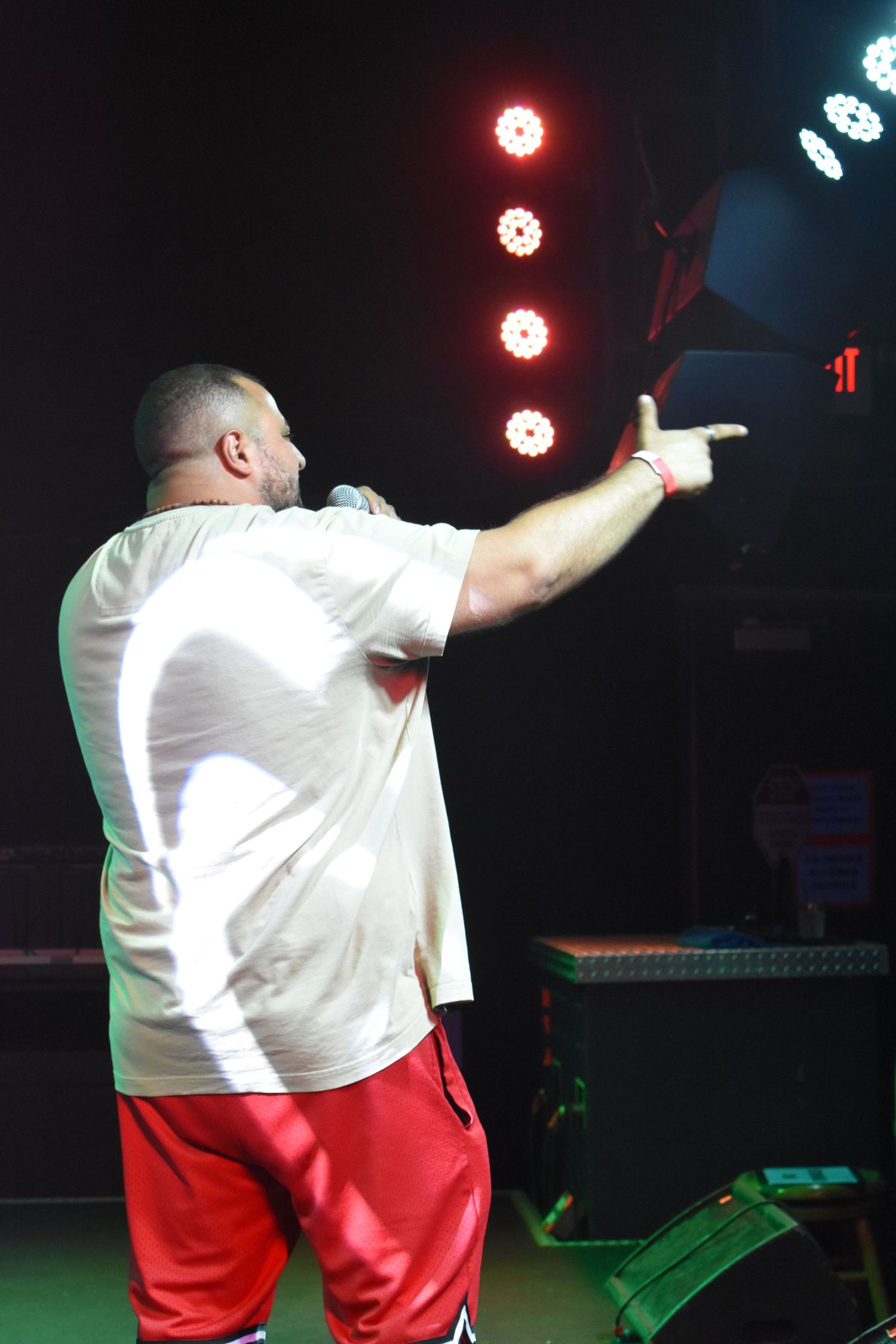 A performer in a white shirt and red shorts points to the crowd while holding a microphone on stage.