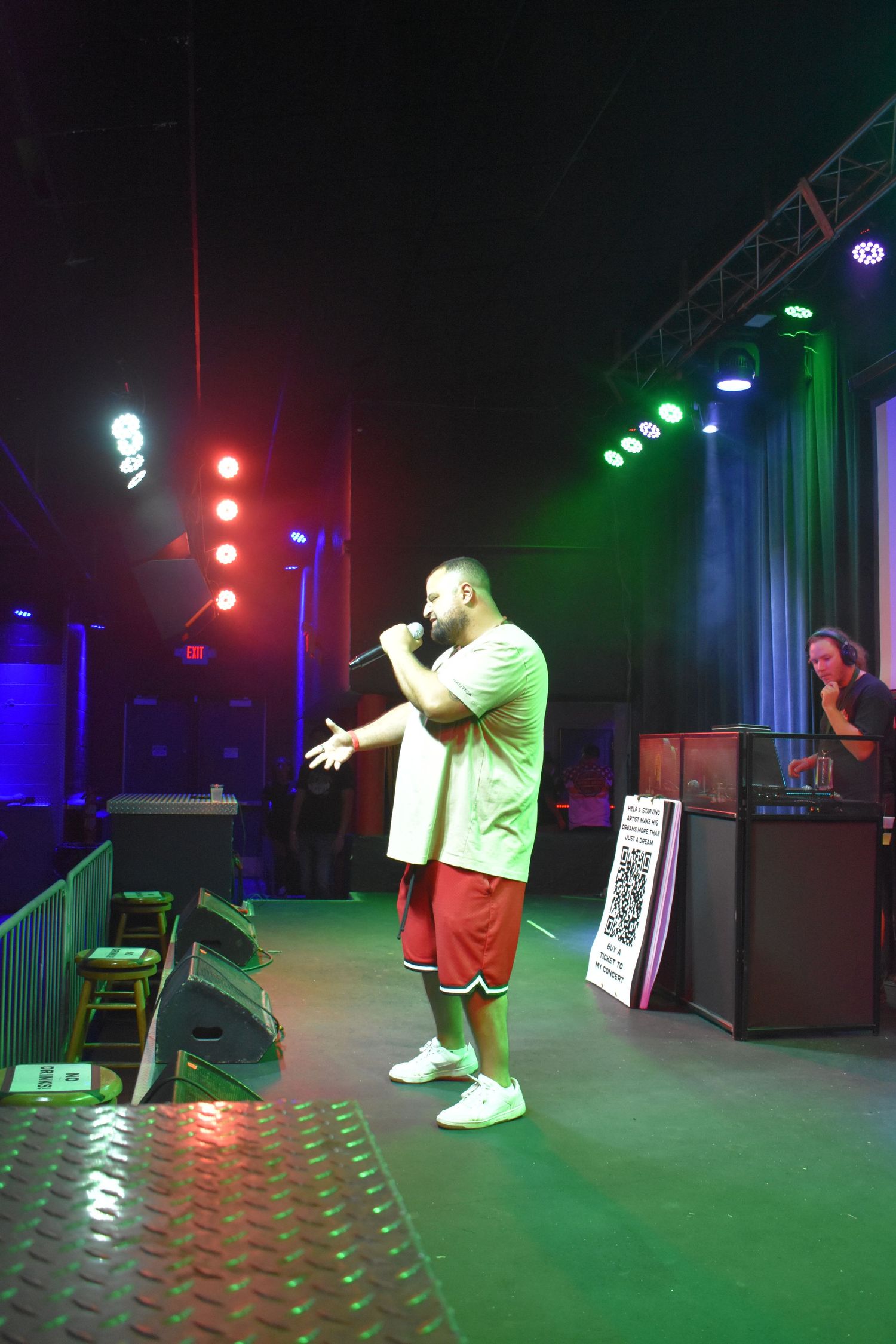A male rapper performs on stage with colorful lights and a DJ visible in the background.
