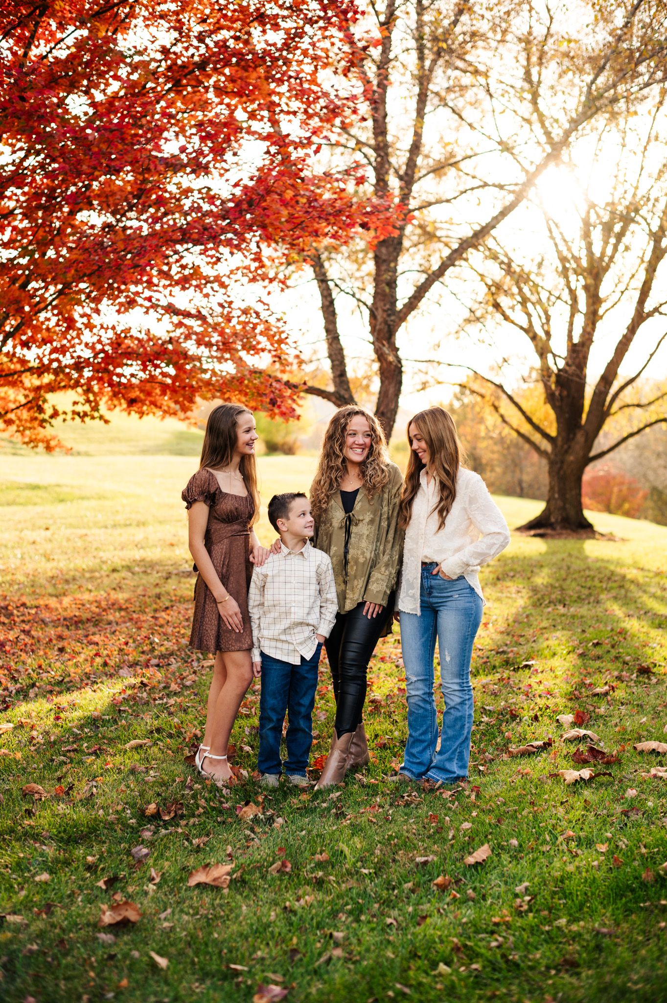 Family of four posing outdoors in autumn, surrounded by vibrant red and orange fall foliage during golden hour.