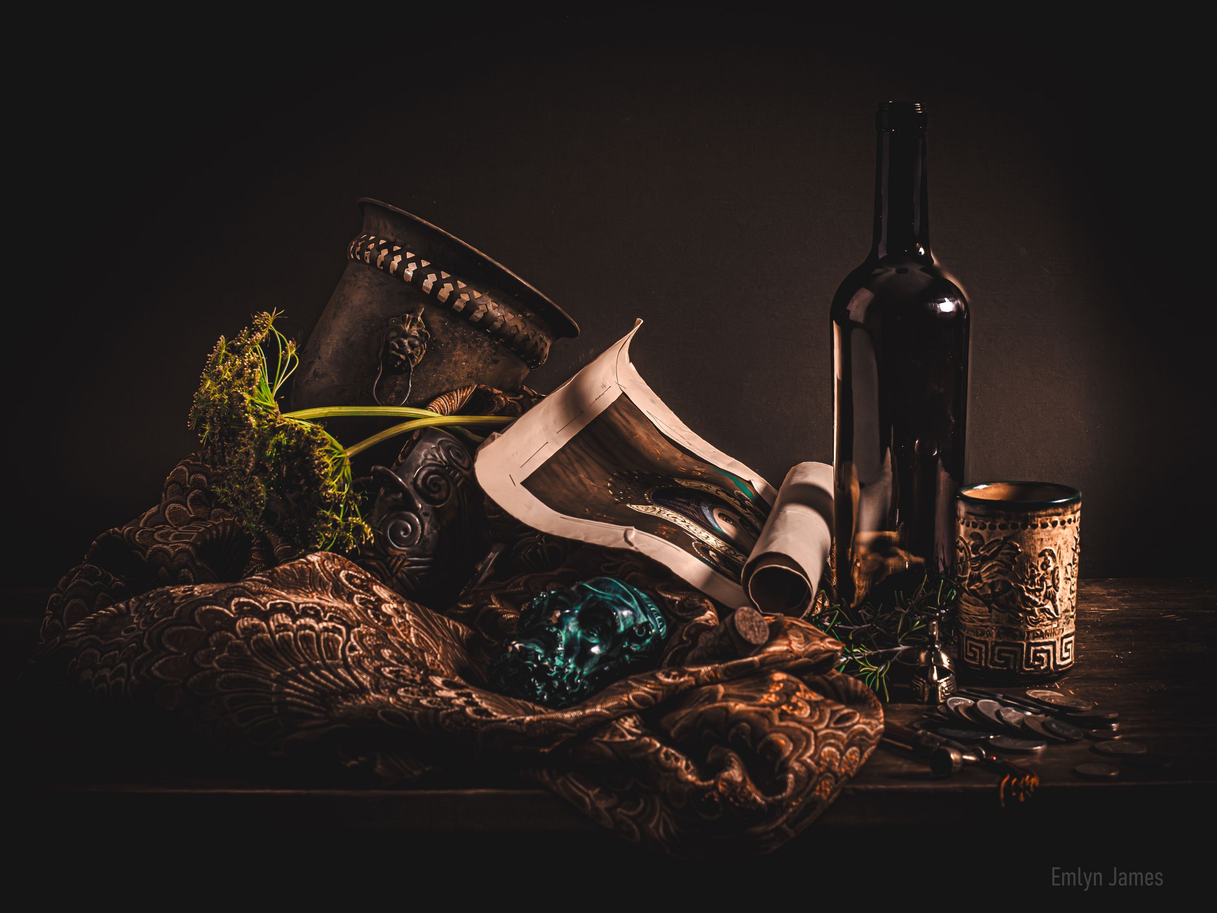 Dark still life with wine bottle, scroll, ornate cup, leather hat, green plant, and blue glass orb on rustic wooden table.