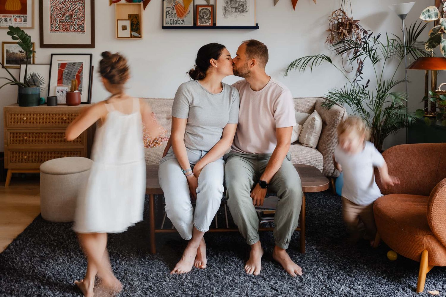 Parents s'embrassent sur le canape quand leurs enfants courent et jouent autour d'eux, un instant de vie ordinaire qui prendra tout son sens