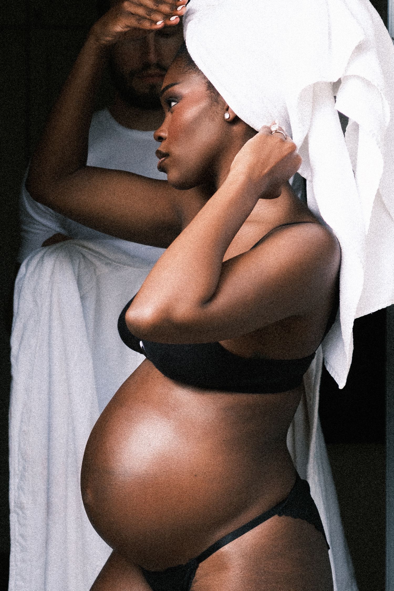 Pregnant woman in white shirt and jeans with partner's hands gently cradling her bare baby bump.