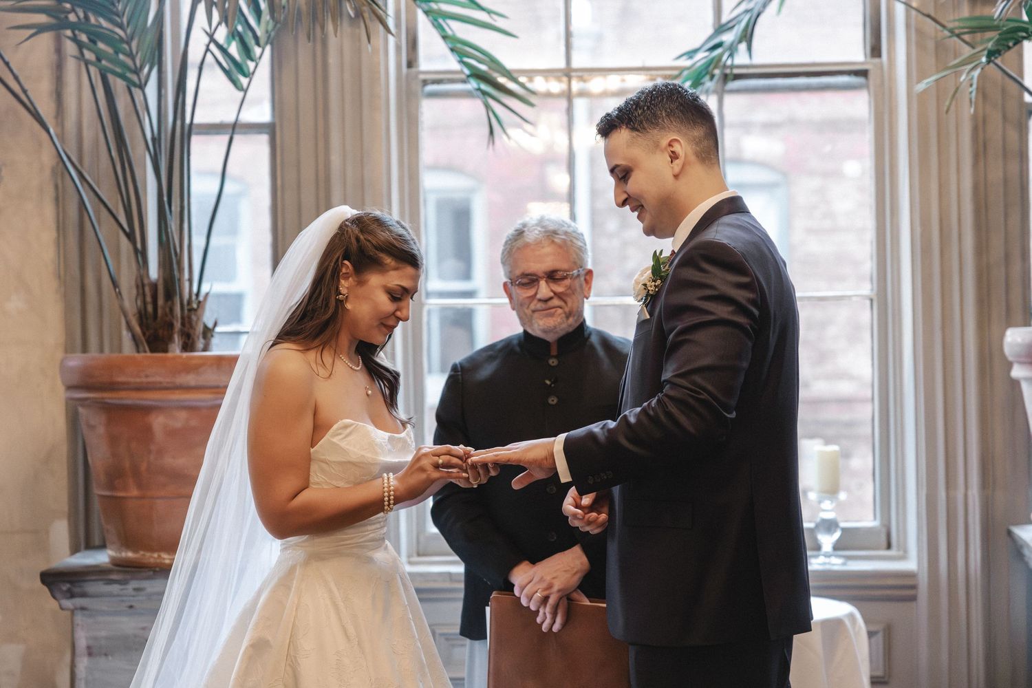 Bride and groom exchanging rings during wedding ceremony with officiant in elegant venue.