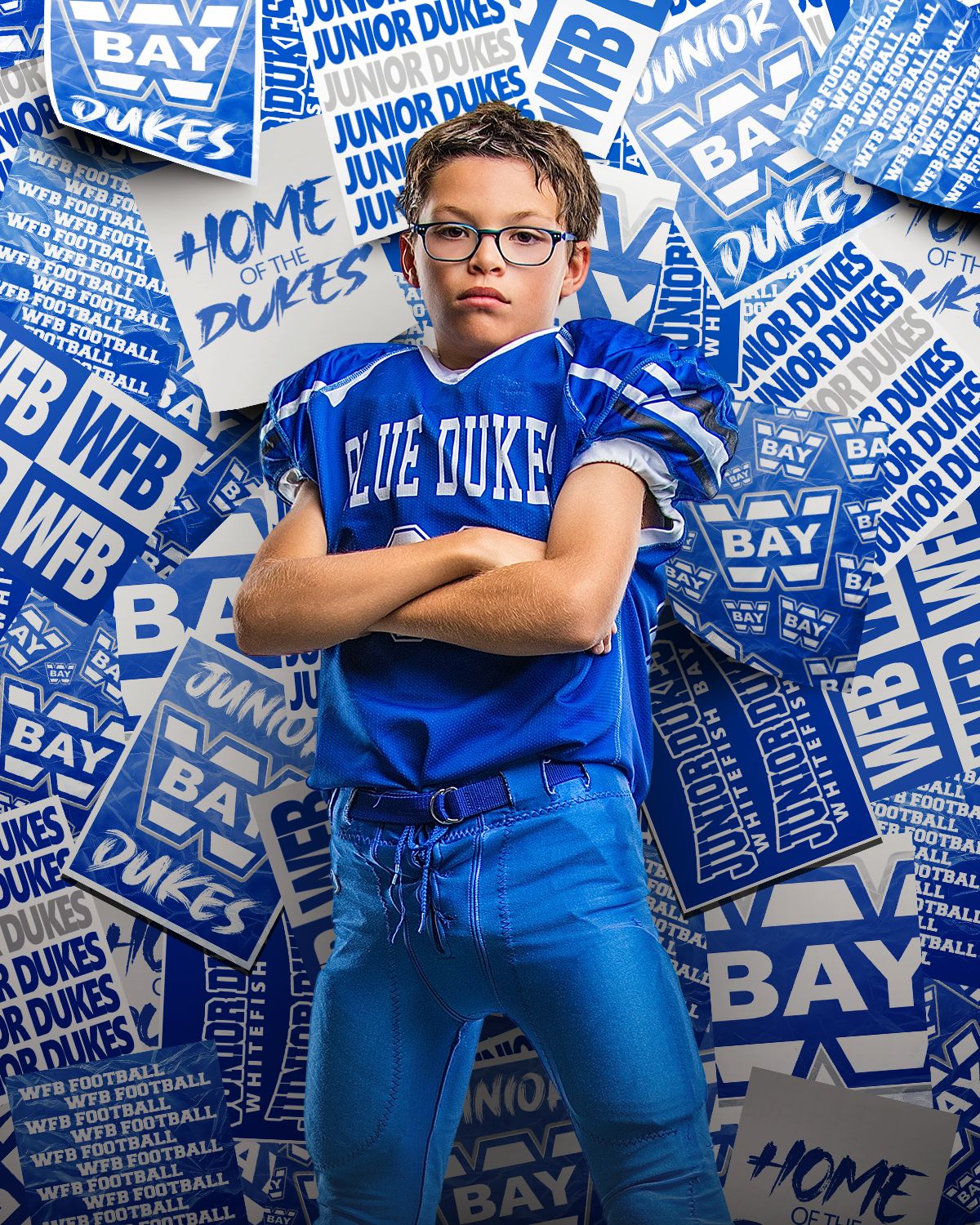 Young football player in Blue Dukes jersey poses confidently with arms crossed against a backdrop of team signs.