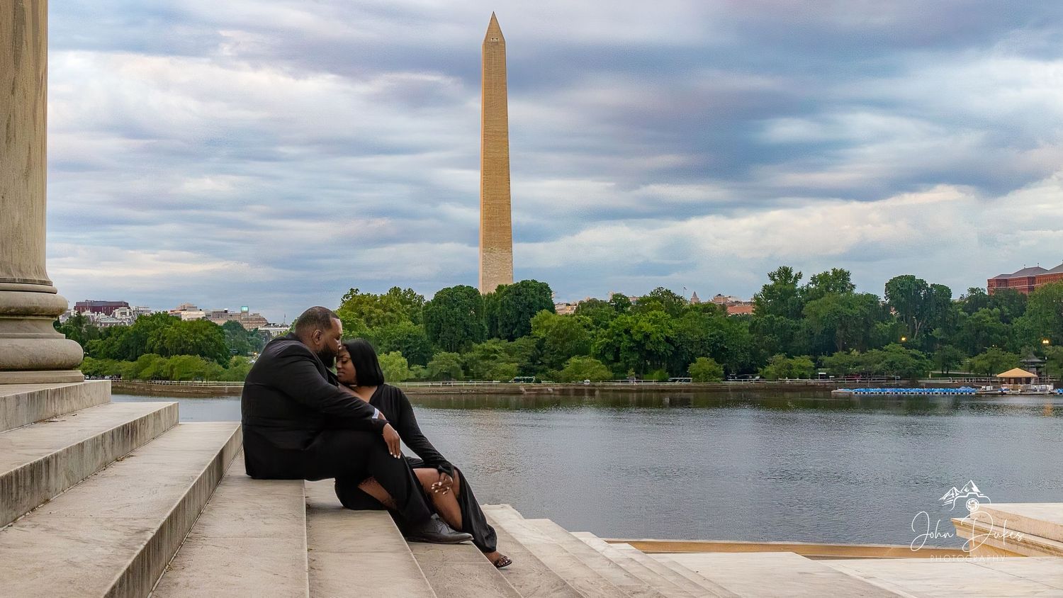 Couple sitting on steps near the Tidal Basin with Washington Monument in background on a cloudy day.