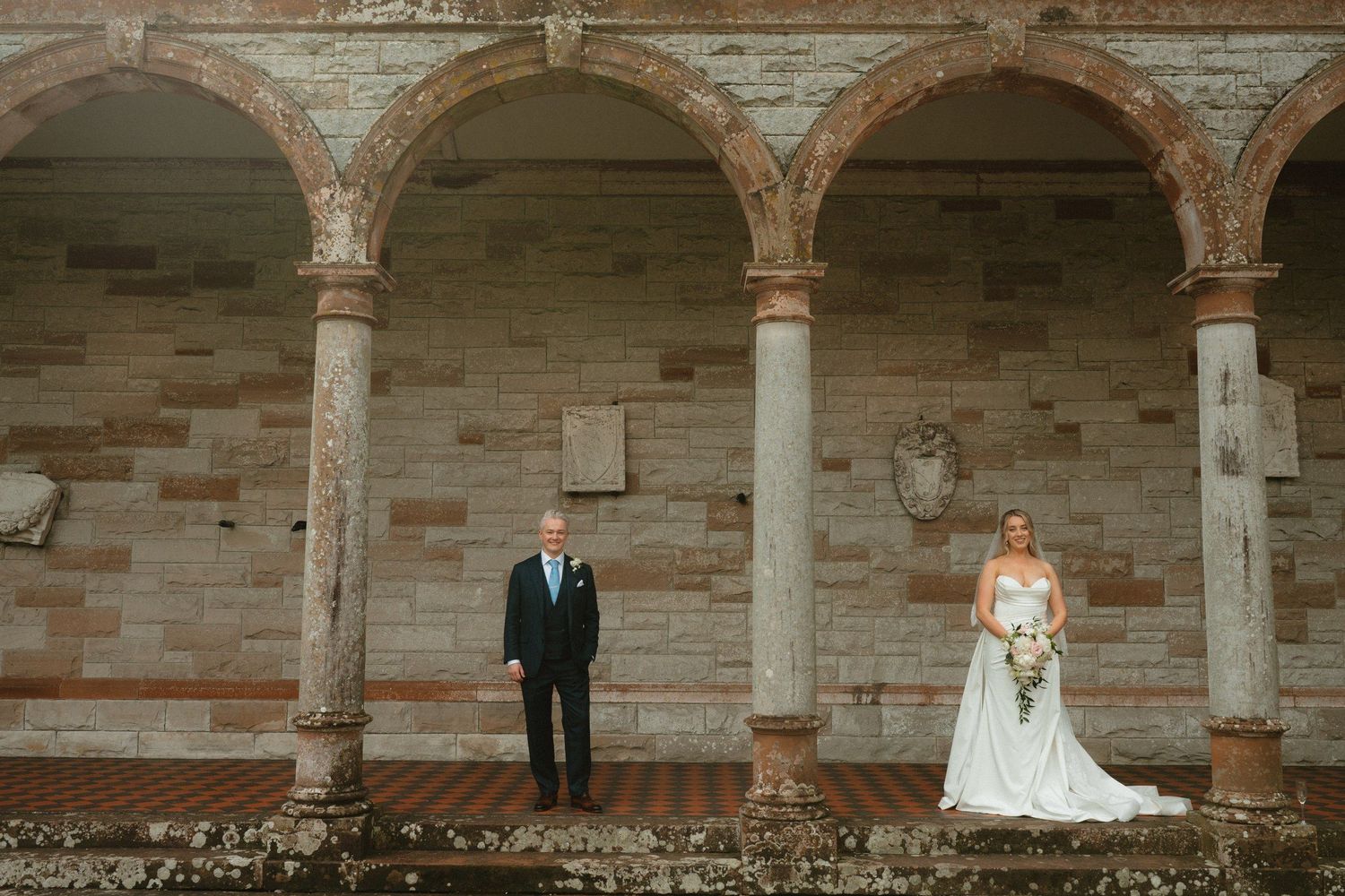 Wedding couple framed by stone arches at Castle Leslie Estate.