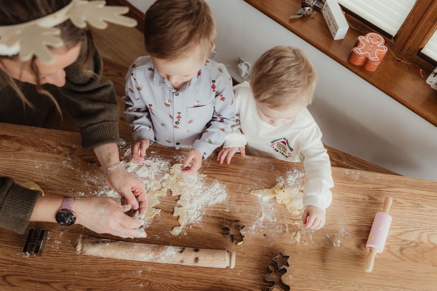 Two children and an adult making Christmas cookies with dough and cookie cutters on a wooden table.