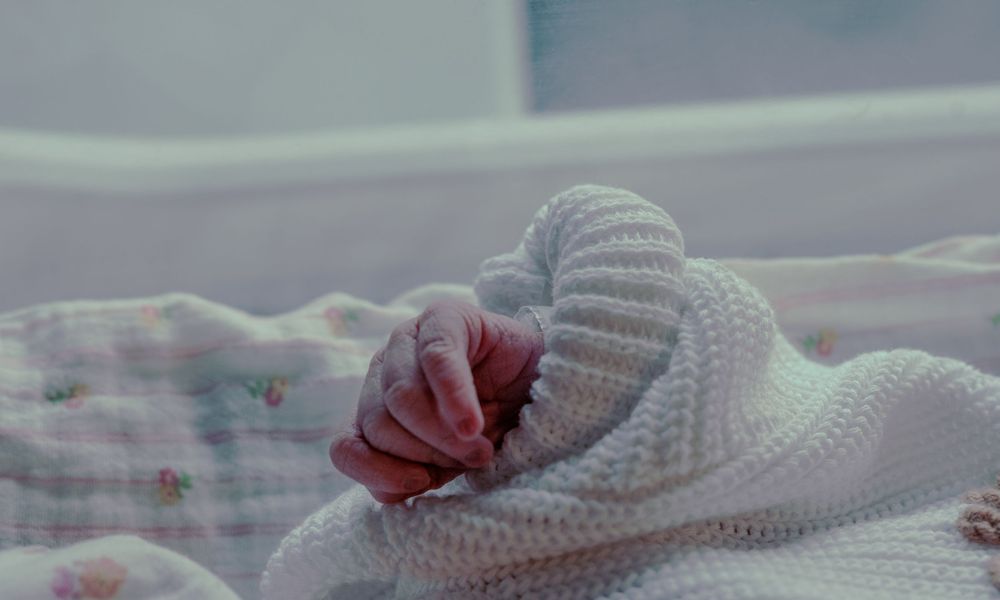 Close-up of sleeping newborn baby hand resting on soft knit white blanket in hospital.