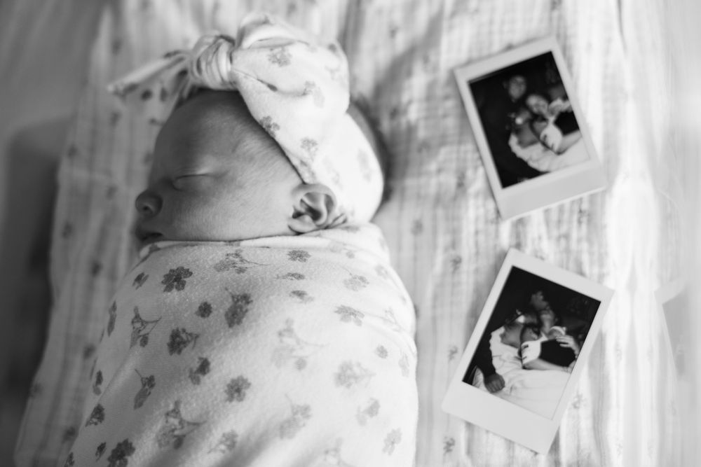 Black and white photo of swaddled newborn baby with headband bow beside Polaroid photos.