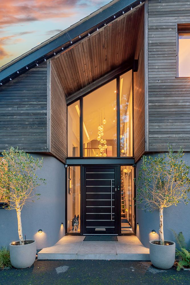 Modern home exterior entrance with wood cladding and large glass door at dusk.