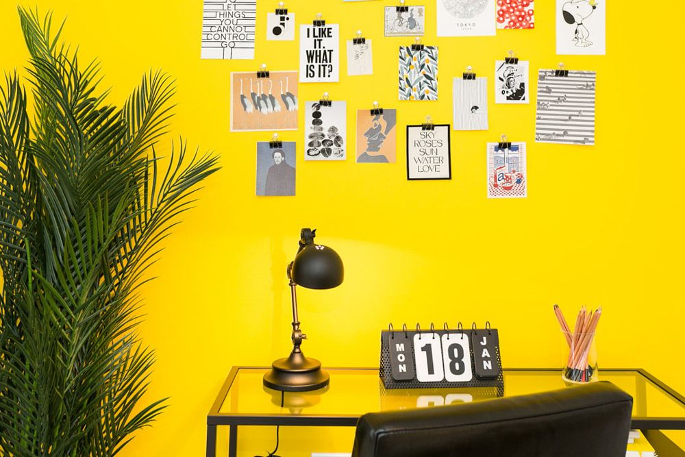 Bright yellow home office with desk, lamp, calendar, and colorful mood board wall art.