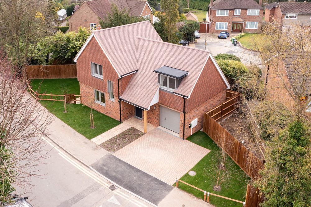 Aerial view of modern red brick detached house with garage and landscaped garden.