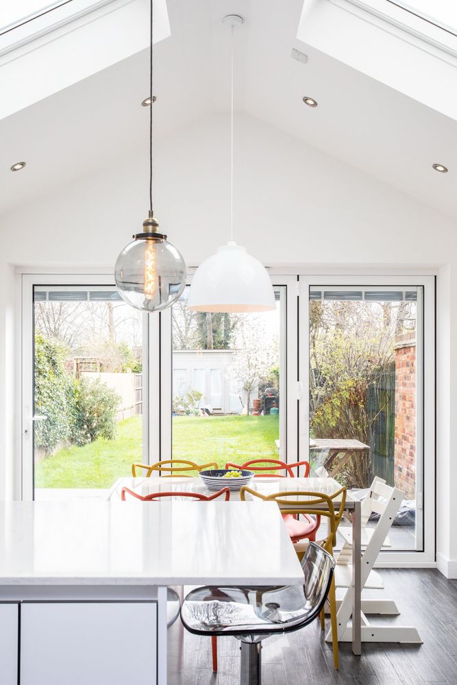 Bright white kitchen dining area with pendant lights and garden view through glass doors.