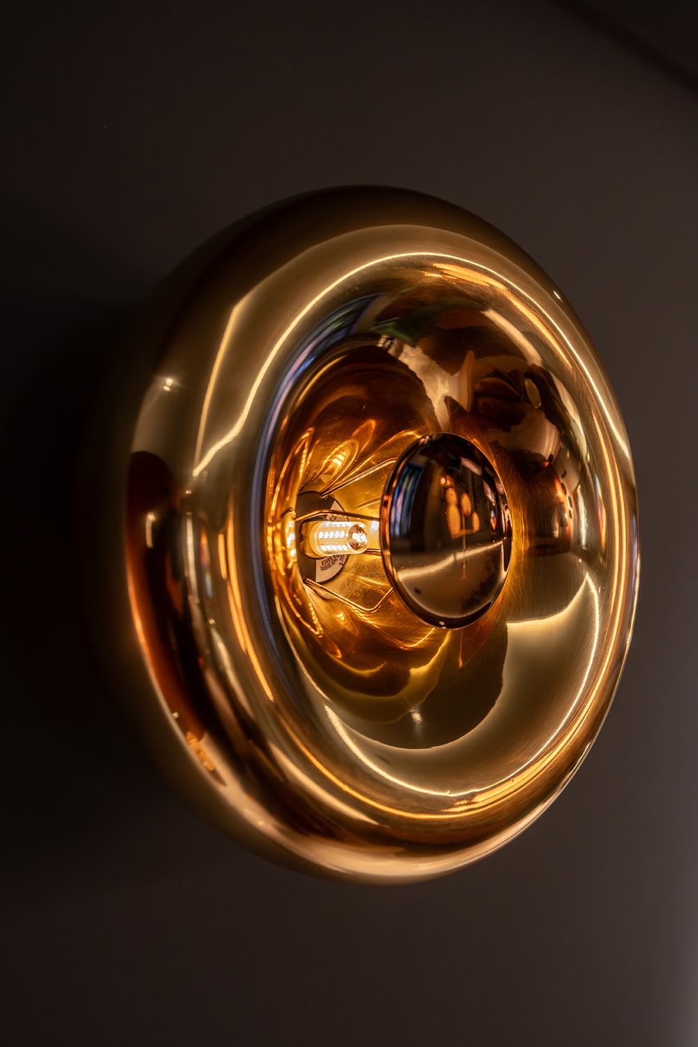 Decorative gold metallic circular wall light fixture with warm glowing bulb.