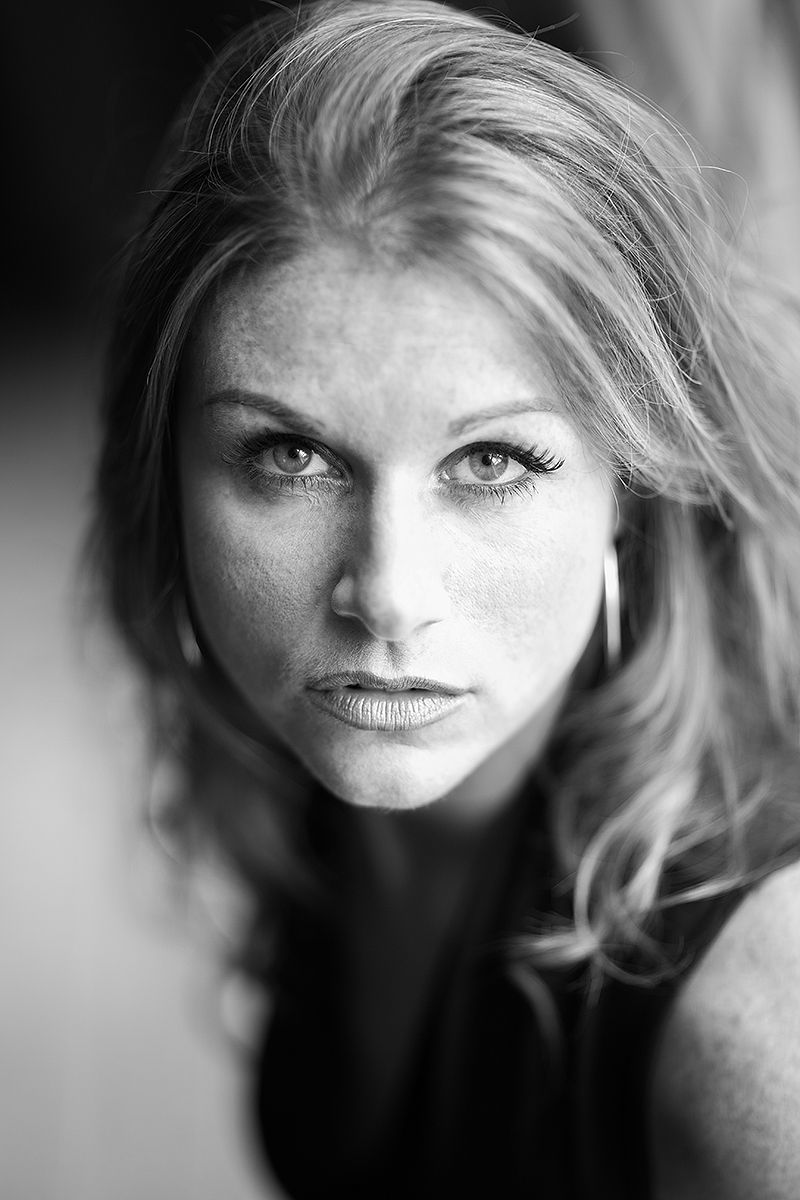 Black and white portrait of blonde woman with freckles and intense gaze outdoors.