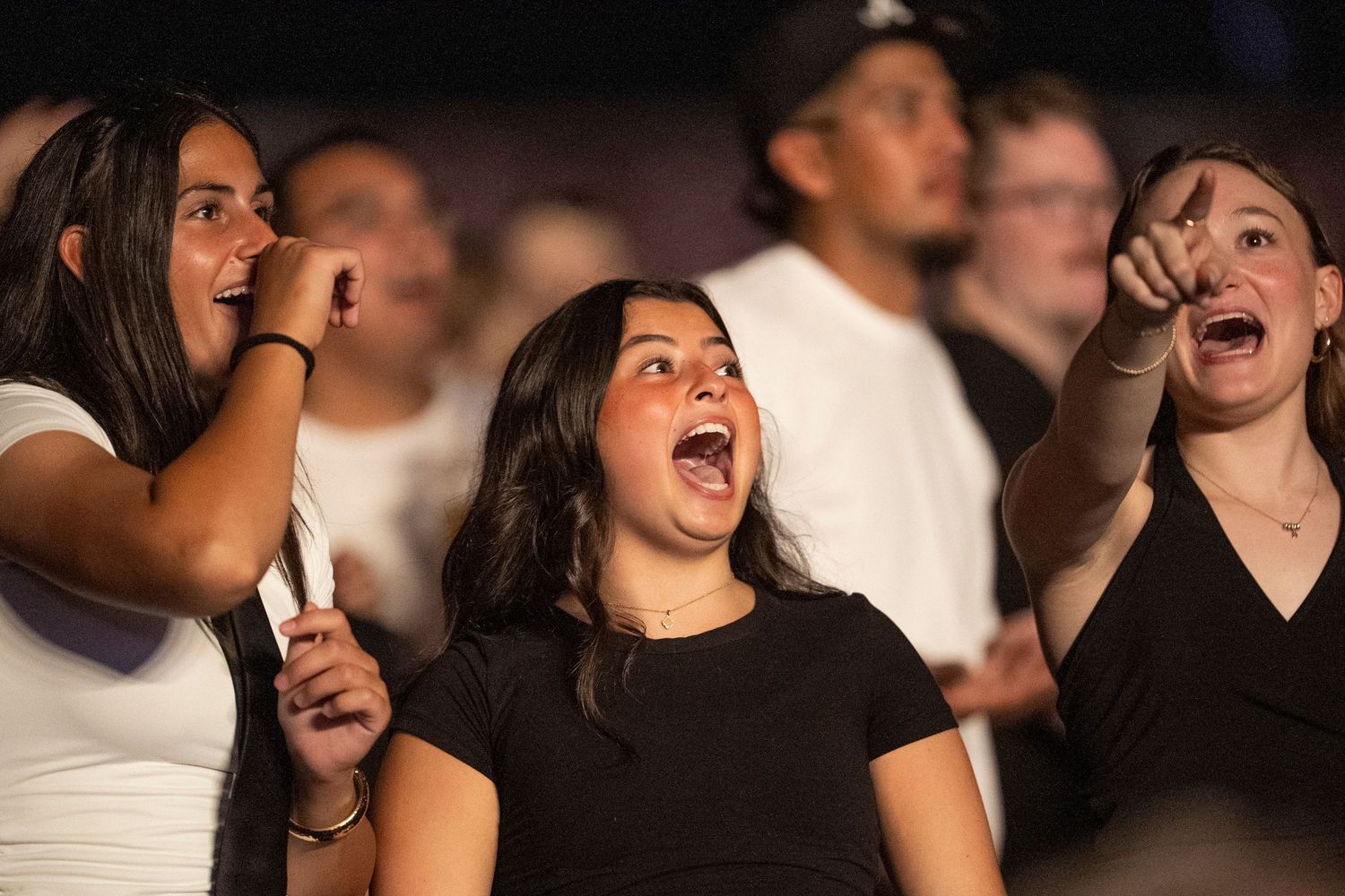 Excited young women cheering and reacting with open mouths at a live event or concert.