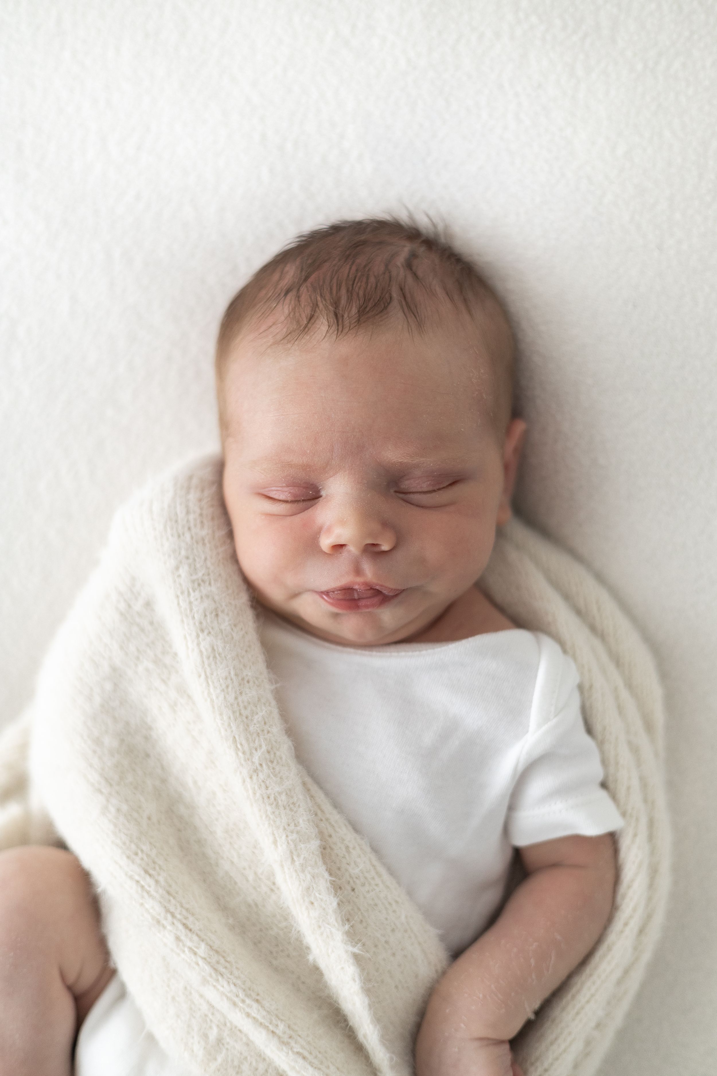 Newborn baby peacefully wrapped in a soft neutral blanket at a cosy Nottingham photography studio