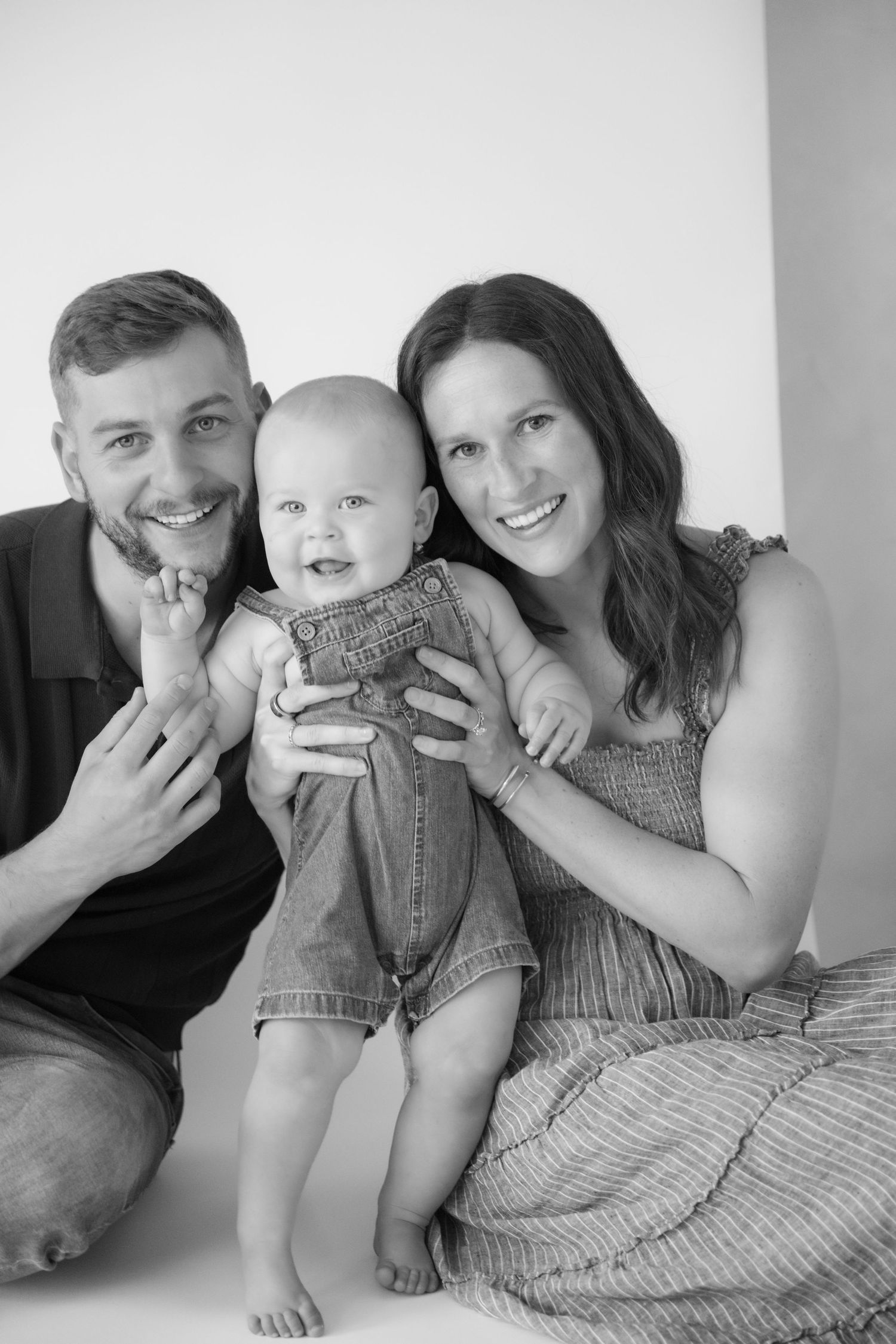 Parents and their one year old smile at the camera during an in-studio family session in New Richmond, WI.