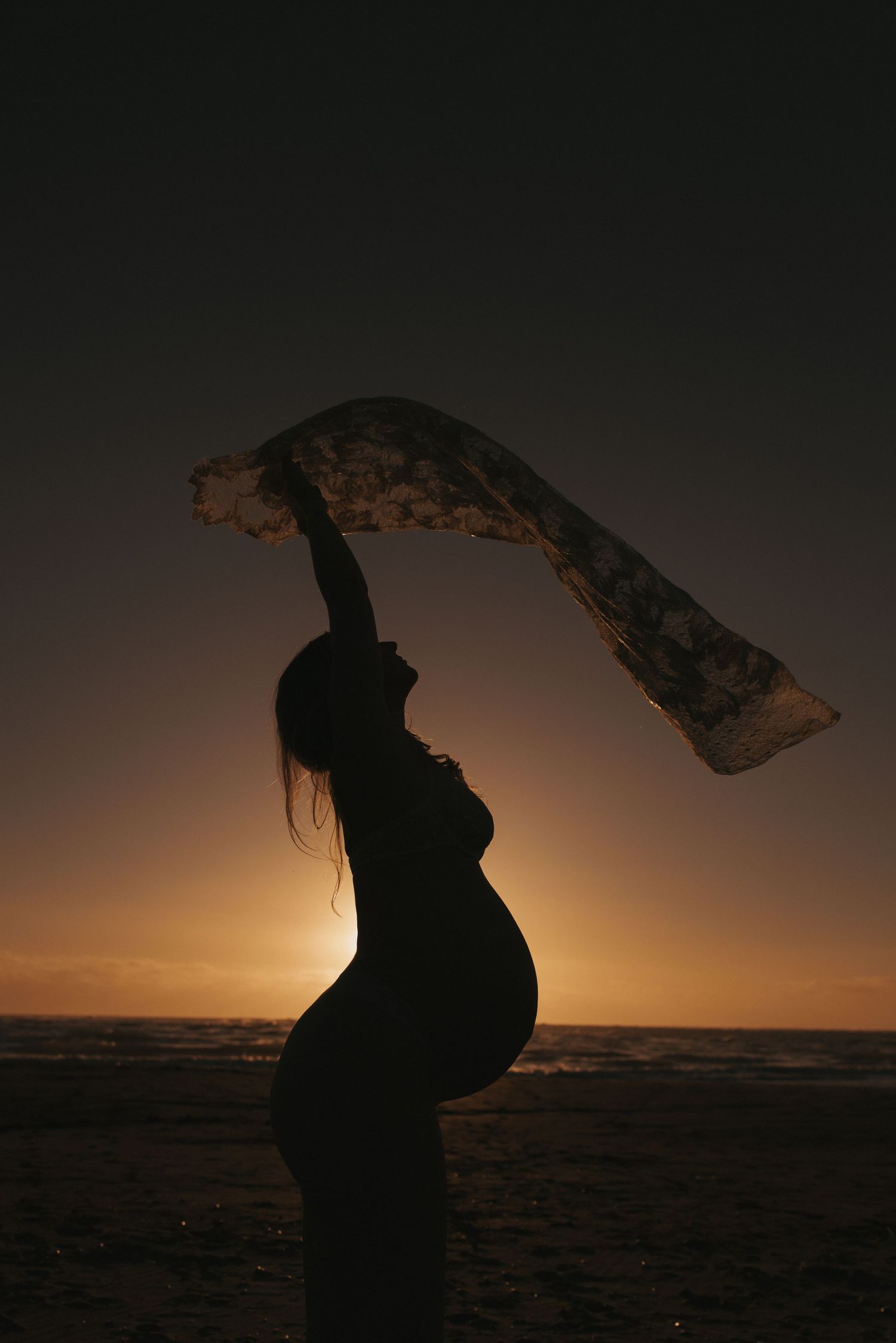 Silhouette of a pregnant woman in Raglan beach New Zealand at Golden Hour captured by Nami Creative.