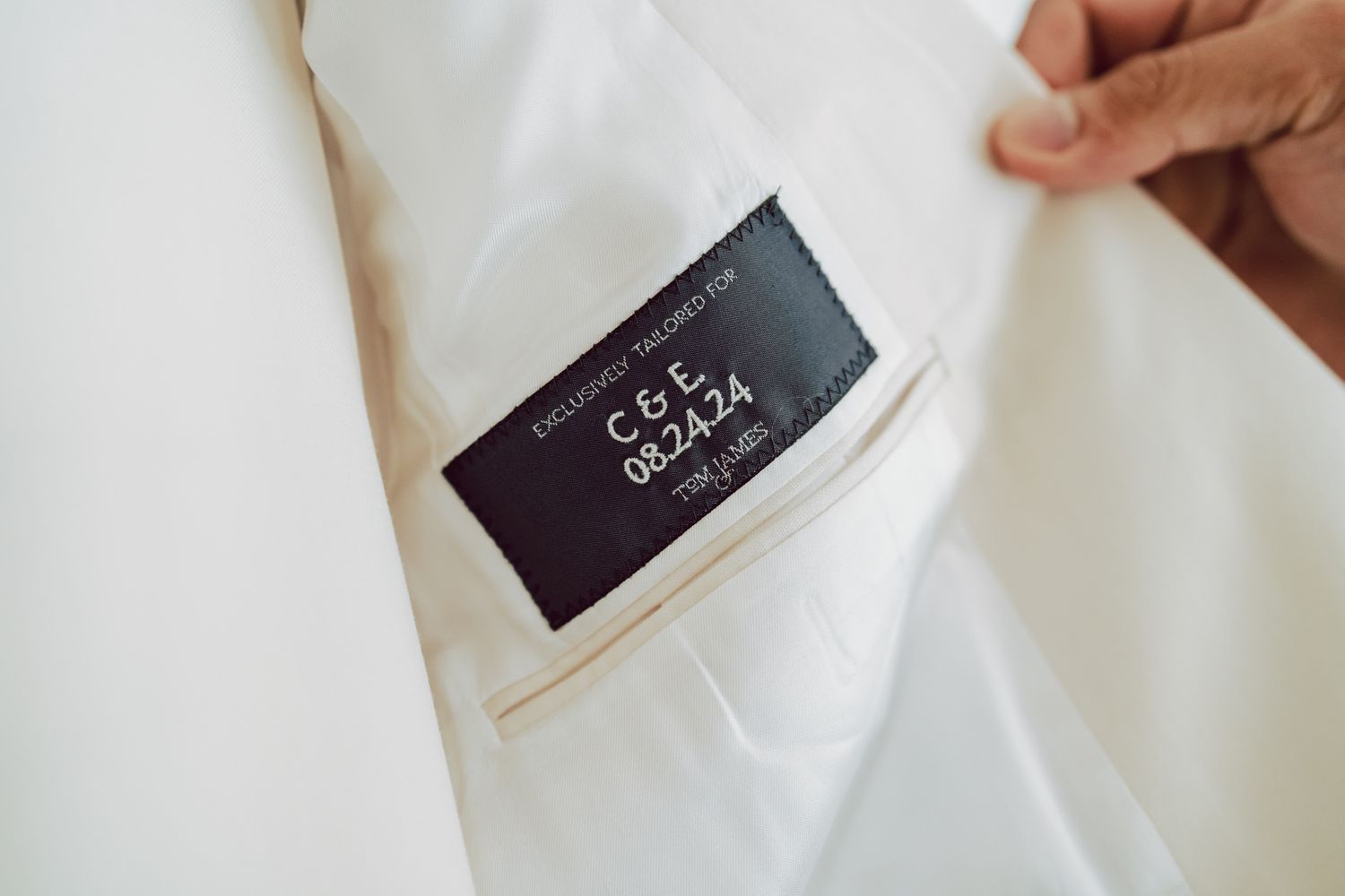 Custom black label inside white suit jacket with initials C&E and date 08.24.24, personalized wedding attire detail.