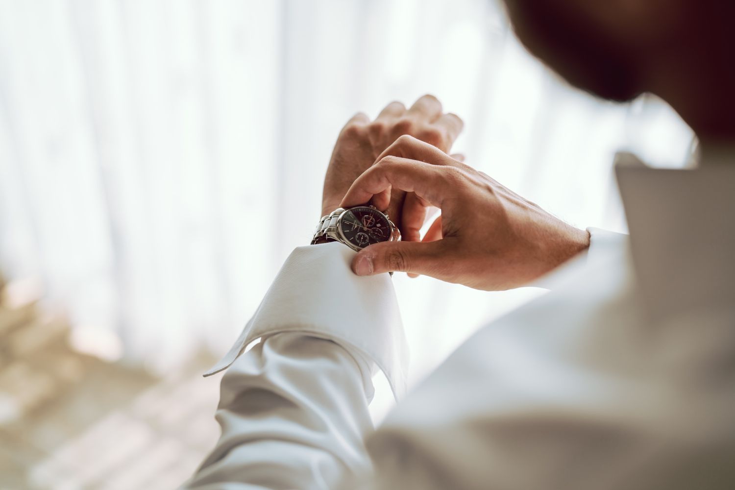 Man in white dress shirt checking luxury wristwatch, close-up shot with soft natural light.