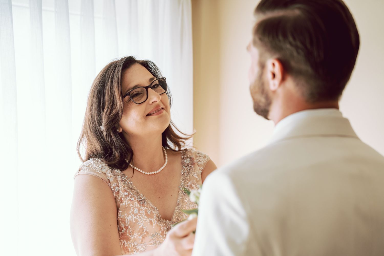 Bride in lace dress and glasses smiling warmly at groom during wedding ceremony.