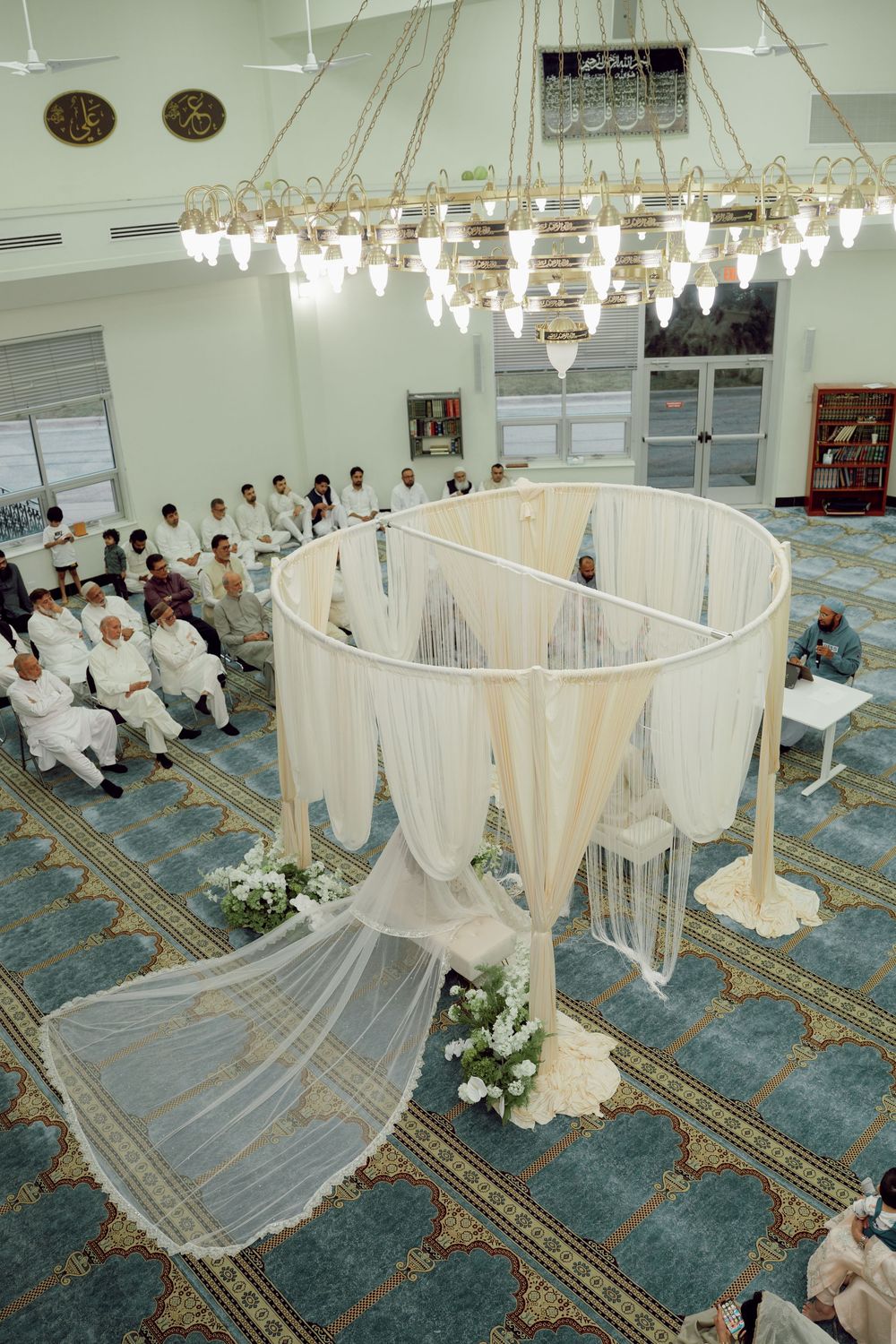 Elegant Islamic wedding ceremony setup with white draping canopy, floral decor, and guests seated in a mosque.