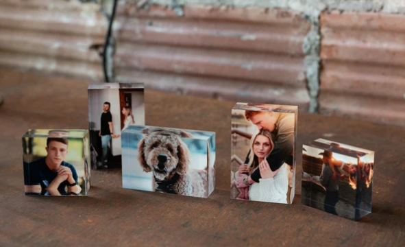 Small acrylic photo blocks displaying portraits of people and a dog, arranged on a rustic wooden surface.