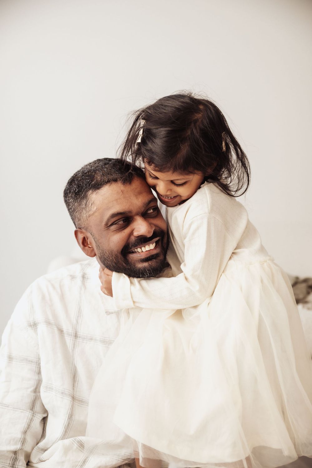 A smiling father in white embraces his young daughter who hugs him warmly.