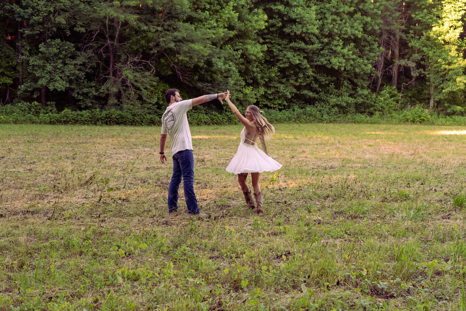 Couple dancing and twirling in a sunlit open meadow surrounded by dense green forest.