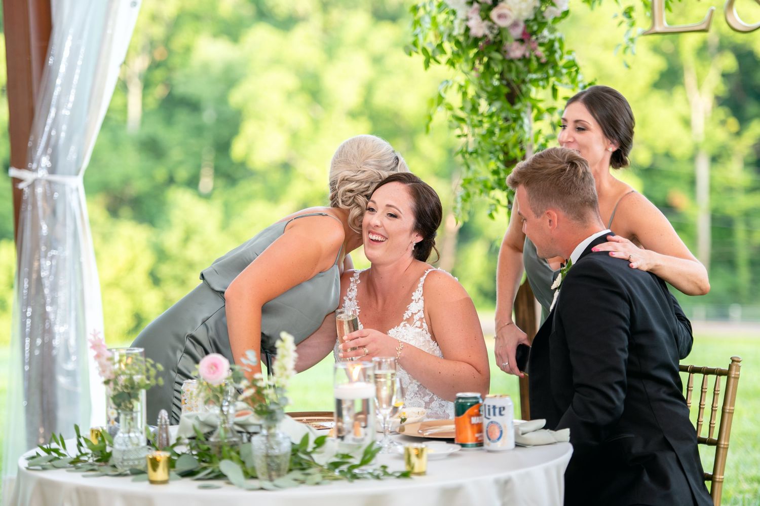 Wedding guests laughing and celebrating at elegantly decorated reception table with floral arrangements.