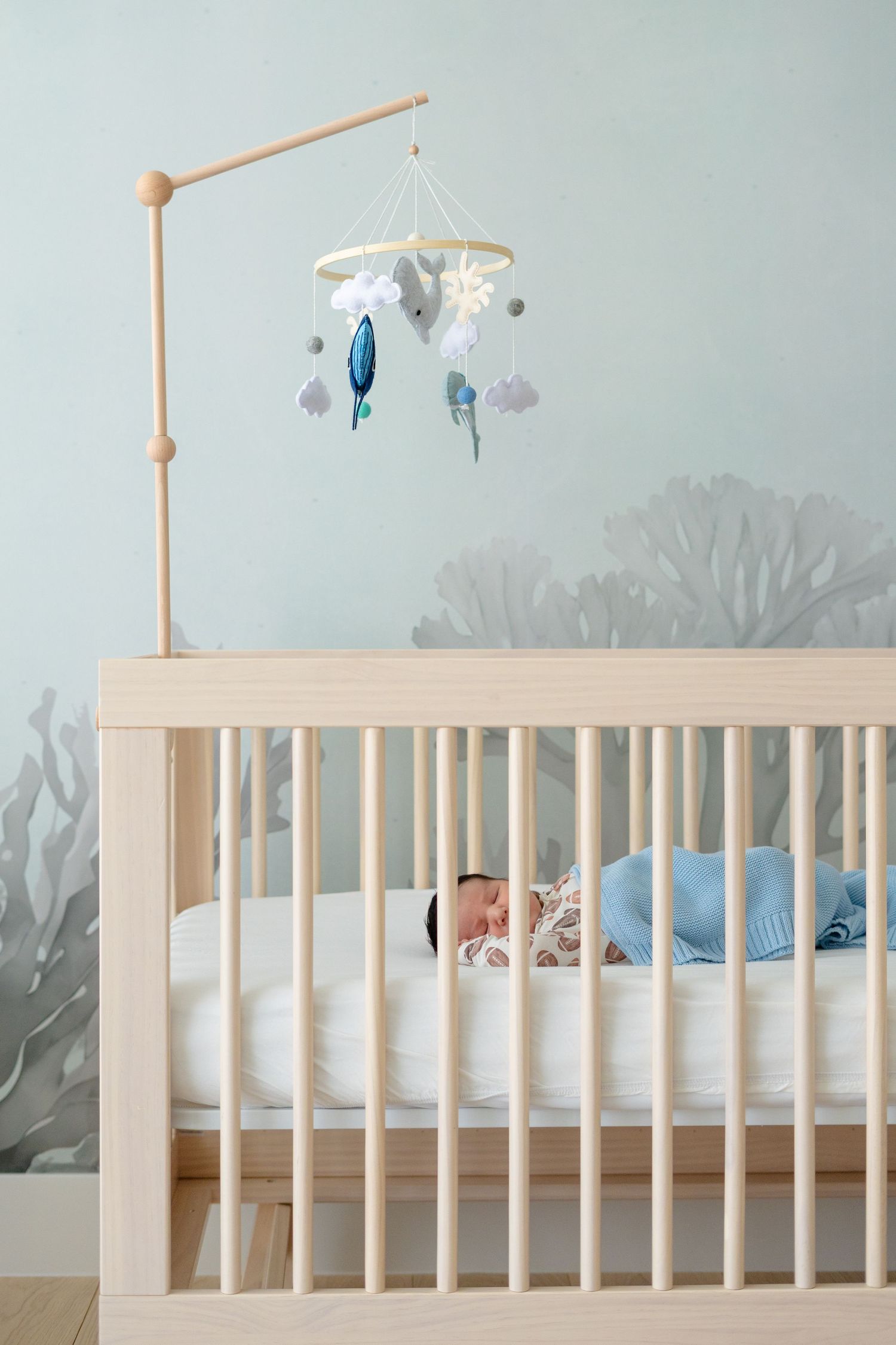 Newborn baby sleeping in a modern wooden crib with an ocean-themed mobile in a serene nursery.